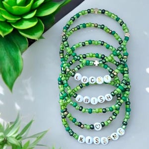 May include: Set of six green beaded bracelets with white letter beads spelling "LUCKY", "IRISH", and "KISS ME". Each bracelet has a gold charm.