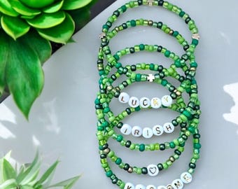 May include: Set of six green beaded bracelets with white letter beads spelling "LUCKY", "IRISH", and "KISS ME". Each bracelet has a gold charm.