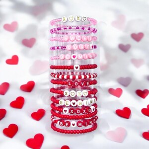 May include: A stack of colorful beaded bracelets with Valentine's Day themed messages, including "Sweet", "XOXO", "Be Mine", "Love", and "XOXO".