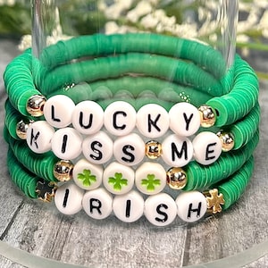 May include: A set of three green beaded bracelets with white letter beads spelling "LUCKY KISS ME IRISH". The bracelets are decorated with gold beads and shamrock charms.
