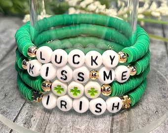 May include: A set of three green beaded bracelets with white letter beads spelling "LUCKY KISS ME IRISH". The bracelets are decorated with gold beads and shamrock charms.