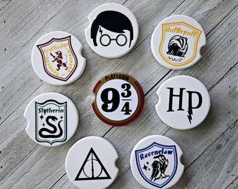 May include: Set of 9 round white ceramic coasters with various Harry Potter themed designs. The designs include the Hogwarts houses Gryffindor, Hufflepuff, Slytherin, and Ravenclaw, as well as the Platform 9 3/4 sign, the Harry Potter logo, and a silhouette of Harry Potter wearing glasses.