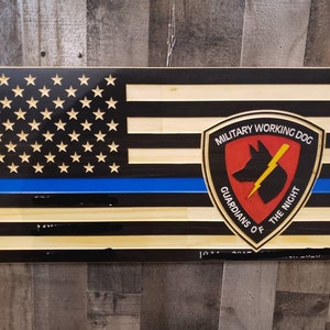 May include: Wooden American flag with a blue line and a military working dog emblem. The emblem is red, black, and yellow with the text "Military Working Dog, Guardians of the Night".