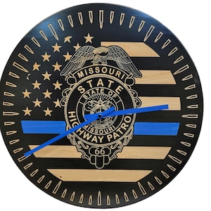 May include: A black and brown wooden clock with a blue line and the words "Missouri State Highway Patrol" and "66" on the face. The clock has a design of an American flag with stars and stripes.