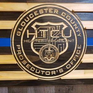 K&ouml;nnte beinhalten: Amerikanische Flagge aus Holz mit blauem Streifen und rundem Emblem. Das Emblem lautet "Gloucester County Prosecutor's Office" und "High-Tech Crimes Unit."
