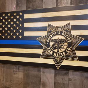 May include: A wooden American flag with a blue line, representing law enforcement, and a sheriff's badge with the text "Sheriff's Office San Mateo Co."
