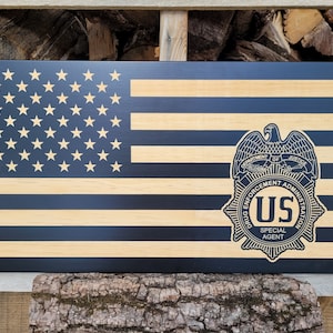 May include: A wooden American flag with a black and gold DEA badge. The badge features an eagle, the words "Department of Justice", "Drug Enforcement Administration", "US", and "Special Agent".