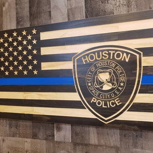 May include: A wooden American flag with a blue line, featuring a carved Houston Police Department badge with the text "HOUSTON, CITY OF HOUSTON POLICE, SPACE CITY U.S.A., POLICE".
