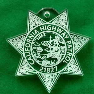 May include: A white acrylic star-shaped ornament with the words "California Highway Patrol" and the number "21827" inscribed on it. The ornament features a detailed design of the California state seal.