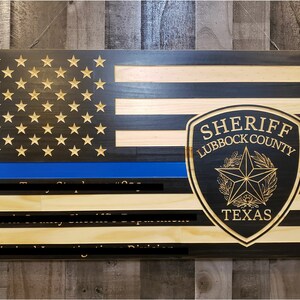May include: A wooden American flag with a blue line, a sheriff's badge, and the text "SHERIFF LUBBOCK COUNTY TEXAS".