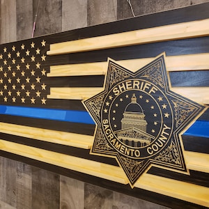 May include: A wooden American flag with a blue line, a sheriff's star, and the words "Sheriff Sacramento County" in gold lettering.