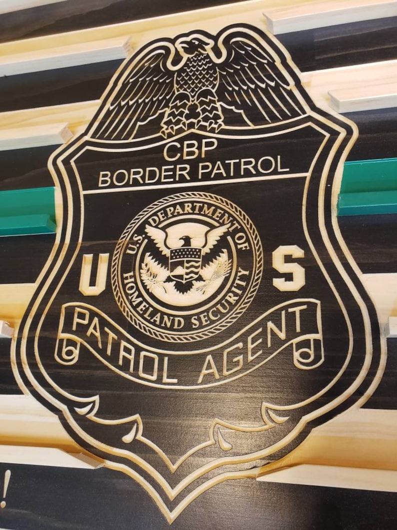 May include: Wooden plaque featuring a CBP Border Patrol badge design. The badge is black with a detailed border and engraved text, including "CBP Border Patrol," "U.S. Department of Homeland Security," and "Patrol Agent." An eagle tops the badge.