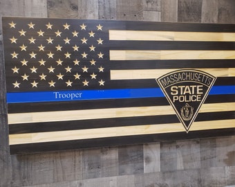 Könnte beinhalten: Amerikanische Holzflagge mit blauer Linie, dem Wort "Trooper" und dem Emblem der "Massachusetts State Police". Die Flagge hat geschnitzte Sterne und abwechselnd schwarze und natürliche Holzstreifen.