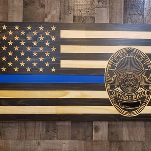 May include: A wooden American flag with a blue line and a carved police badge that says "Sergeant Ontario Police".