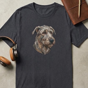 Pode incluir: Uma t-shirt de manga curta em cinzento-carvão escuro com uma ilustração gráfica detalhada de um cão de pelo desgrenhado no peito. O cão tem pelo castanho, bronzeado e cinzento com um nariz escuro e olhos expressivos na parte da frente.