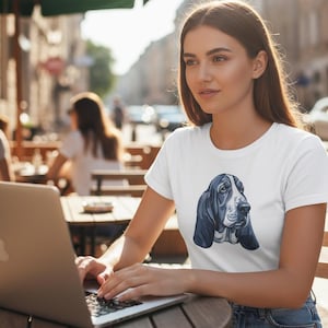 Könnte beinhalten: Weißes T-Shirt mit einer Aquarell-Illustration des Gesichts eines Basset Hounds in Blau- und Grautönen. Die langen Ohren und Augen des Hundes sind deutlich sichtbar. Das T-Shirt hat einen klassischen Rundhalsausschnitt.