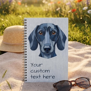 Puede incluir: Un cuaderno con espiral con una ilustración de perro salchicha en la portada. El perro está representado en tonos azules. El cuaderno tiene el texto "Your custom text here". Un sombrero de paja y gafas de sol están cerca.