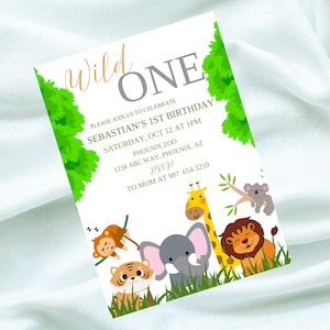 Può includere: Un invito bianco con fogliame verde e un titolo "Wild One" grigio e arancione. L'invito è per il primo compleanno di Sebastian allo zoo di Phoenix il 12 ottobre alle 13:00. L'invito presenta un'illustrazione di cartoni animati di una giraffa, un elefante, una tigre, una scimmia e un koala.