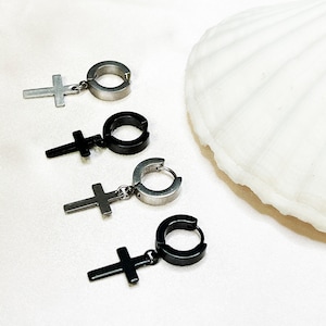 Peut inclure: Quatre paires de boucles d'oreilles créoles argentées et noires avec un pendentif en forme de croix. Les boucles d'oreilles sont présentées sur une surface blanche.