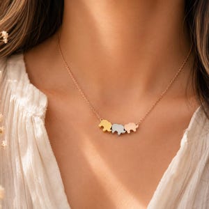 May include: A delicate necklace featuring three small elephant-shaped charms suspended from a thin chain. The charms are finished in three distinct metallic tones: a yellow gold, a silver, and a rose gold, arranged horizontally in a row.