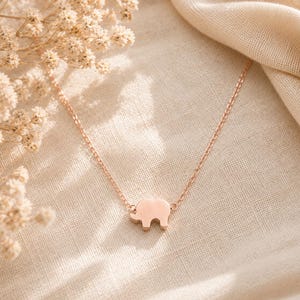 May include: A rose gold-toned necklace featuring a small, flat elephant-shaped pendant centered on a delicate cable chain. The metal has a smooth, polished finish, and the design is simple, showcasing the silhouette of an elephant in profile.