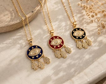 May include: Three gold-colored necklaces with pendants featuring an eye design. Each pendant has a different colored enamel background: blue, red, and black. Below the eye are three small hand-shaped charms, all adorned with small crystals.