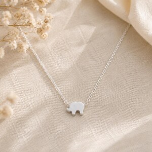 May include: A silver-toned necklace featuring a small, flat elephant-shaped pendant centered on a delicate, thin link chain. The pendant has a smooth, solid surface and is attached directly to the chain on both sides of the elephant figure.