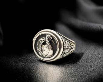 May include: A silver ring with a black onyx stone featuring a detailed dragon design. The ring has a Celtic knot pattern on the band.