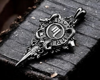 May include: A silver pendant with a detailed design featuring a snake, a circular emblem with the letter "M" inside, and a pointed tip. The pendant is on a dark textured surface.