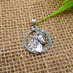 May include: Silver pendant featuring a detailed horse head design with a decorative border. The pendant is on a burlap background.