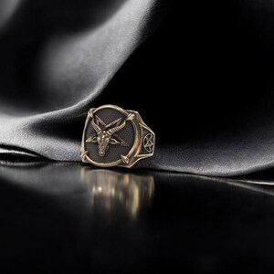 May include: A gold ring with a black enamel design featuring a goat's head with horns and a pentagram.