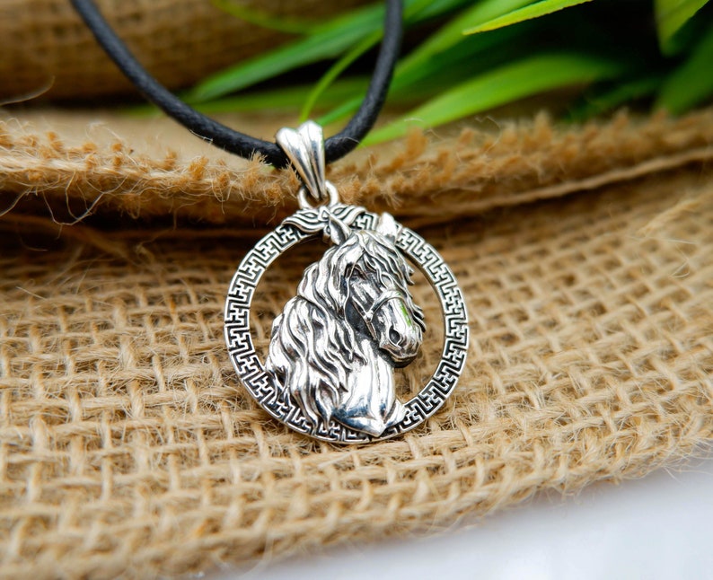 May include: Silver pendant necklace featuring a detailed horse head design surrounded by a Greek key border.