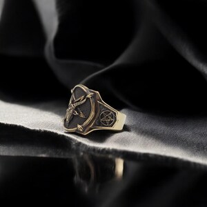 May include: A gold ring with a black enamel design featuring a goat's head and a pentagram.