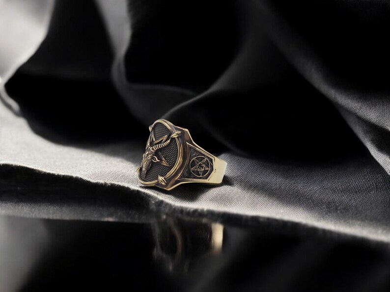 May include: A gold ring with a black enamel design featuring a goat's head and a pentagram.