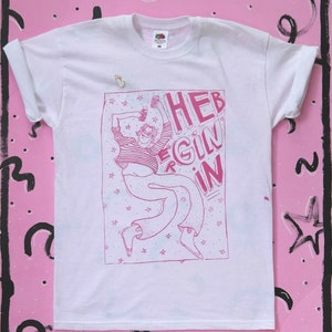 May include: White t-shirt with a pink graphic print of a person jumping with the text "HEB EGIN IN" on a white background.