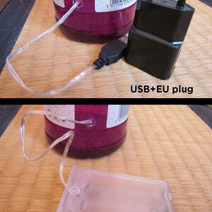 May include: A close-up of a purple glass bottle with a clear string of lights. A black USB plug and a black EU plug are visible. The text "USB+EU plug" is in the image. A clear battery box is also visible. The text "Battery BOX" is in the image.