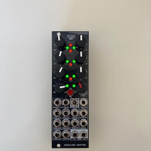 Può includere: Un modulo audio nero con più manopole, pulsanti e jack di ingresso/uscita. Il modulo ha il testo "VICTOR ALPHA XP" e "MODULAIRE MARITIME". Le luci verdi e rosse sono accese sul modulo.