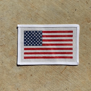 May include: Rectangular needlepoint featuring the American flag. The design includes a blue canton with white stars and red and white stripes. The needlepoint is framed with a white border.