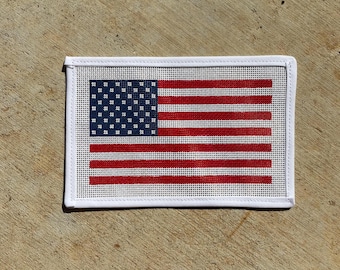 May include: Rectangular needlepoint featuring the American flag. The design includes a blue canton with white stars and red and white stripes. The needlepoint is framed with a white border.