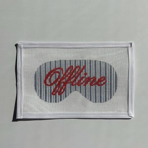 Puede incluir: Máscara para dormir blanca con un diseño de rayas azules y blancas en forma de gafas para dormir. La palabra "Offline" está escrita en rojo en el centro de la máscara. La máscara tiene un borde blanco.