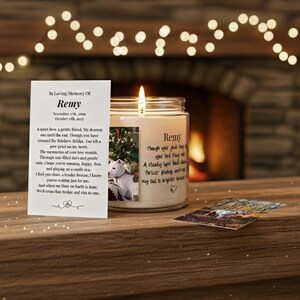 Op de afbeelding: Een brandende kaars in een glazen pot met de naam "Remy" erop, naast een foto van een hond. Een kaart met een gedicht en de woorden "In Loving Memory Of Remy" ligt naast de kaars. Een foto van de hond ligt op tafel.