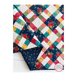 May include: A colorful quilt with a floral pattern. The quilt features a patchwork design with squares of navy blue, white, red, yellow, and teal fabrics. The quilt is adorned with floral patterns and the text "Busy Hands Quilts".