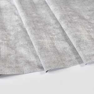 May include: A close-up of a gray fabric with a textured, slightly distressed look. The fabric is folded in several layers, showing the texture and pattern.