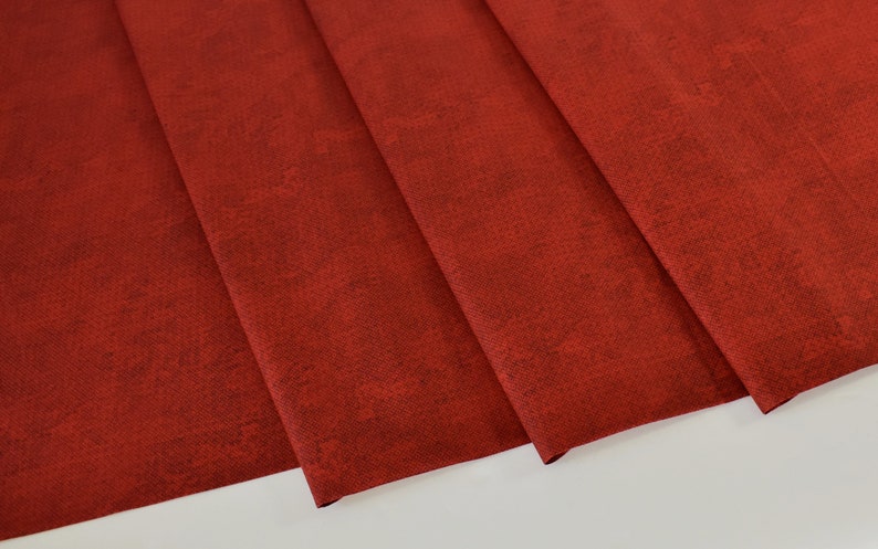 May include: Red fabric with a textured surface. The fabric is folded in a few places, showing the texture and color.