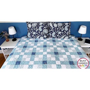 May include: A blue and white patchwork quilt with matching pillow shams. The quilt features a checkerboard pattern with various shades of blue and white squares. The pillow shams have a dark blue paisley design. The image includes the text "BUSY HANDS QUILTS".