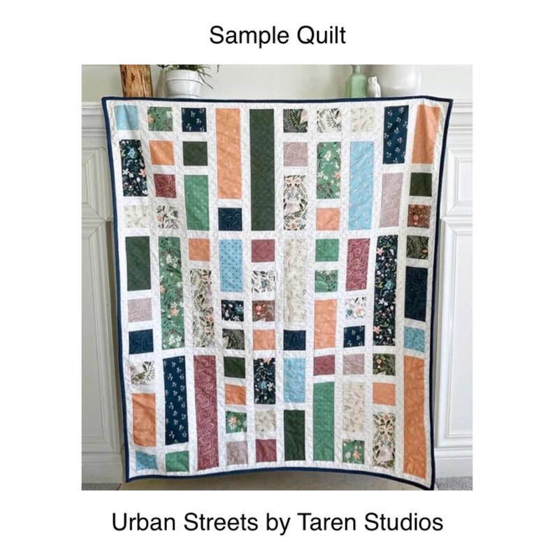 May include: A sample quilt with a geometric pattern in shades of green, blue, orange, and red. The quilt is made up of rectangular blocks with different floral patterns. The quilt is labeled "Urban Streets by Taren Studios".