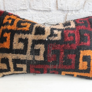 May include: A rectangular cushion with a geometric pattern in shades of black, orange, and red. The cushion is made of a soft, fuzzy material.