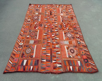 May include: A rectangular textile wall hanging featuring a vibrant orange base with intricate embroidery. The design includes repeating geometric patterns, circular motifs, and triangular shapes in shades of red, white, and dark gray throughout.