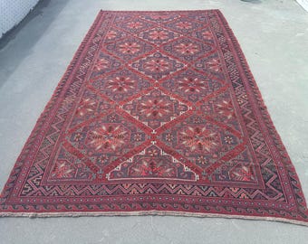 Könnte beinhalten: Ein großer, rechteckiger Teppich mit einem geometrischen Muster in Rot-, Burgunder- und Dunkelblautönen. Das Design zeigt Rautenformen und florale Motive mit einem detaillierten Rand. Der Teppich scheint aus gewebtem Material zu bestehen.