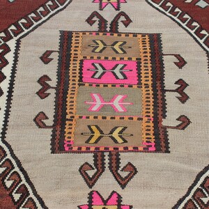 May include: A vintage Turkish rug with a geometric pattern in shades of brown, beige, pink, and orange. The rug has a central medallion with a repeating arrow design.